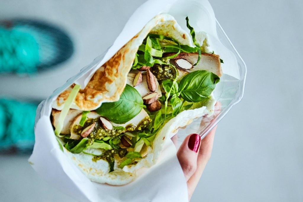 Æggehvidewrap Kvindehånd holder æggehvidewrap med kylling, spidskål, pesto og nødder